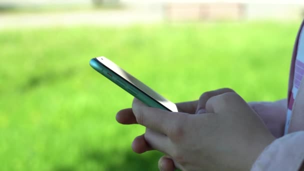 Detailní záběr. Použij v parku smartphone. Žena použití mobilního telefonu v městském parku — Stock video