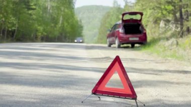 Bozuk bir arabanın önündeki orman yolunda acil durum dur işareti.