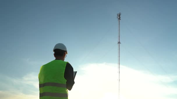 Cellular engineer in a helmet with a tablet and a phone next to the mast. Cellular Inspection — Stock Video