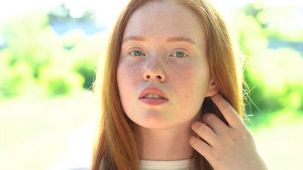 Porträtieren Sie eine lächelnde junge Frau mit roten Haaren und Sommersprossen vor dem Hintergrund einer strahlend sonnigen Wiese. Natürliche Schönheit mit Sommersprossen — Stockfoto