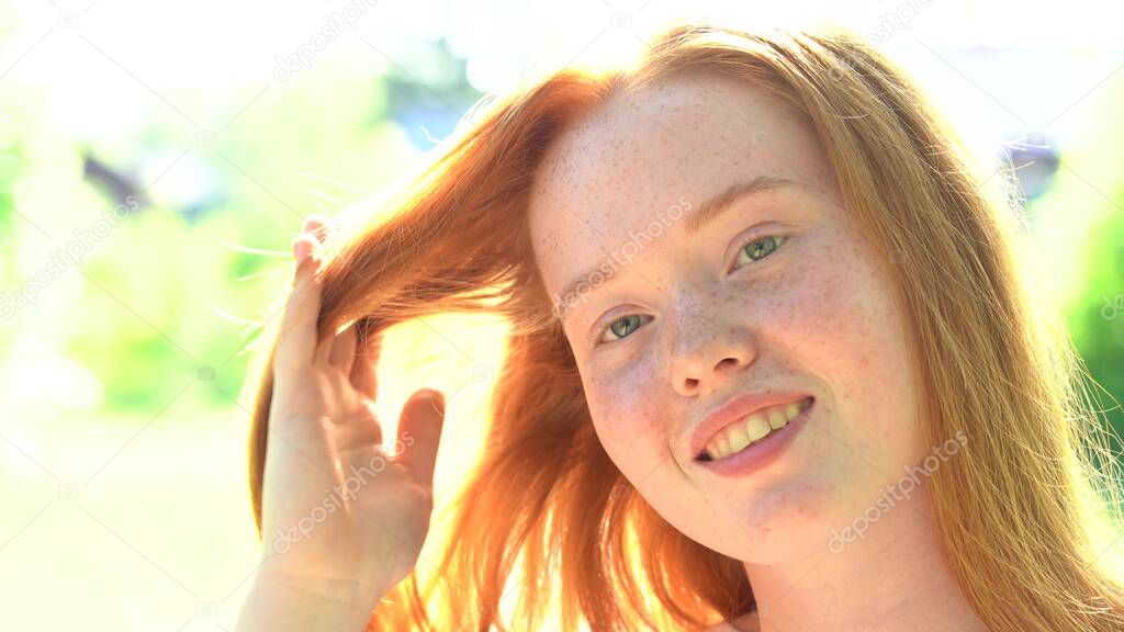 Portrait a smiling young woman with red hair and freckles against the backdrop of a bright sunny meadow. Natural beauty with freckles