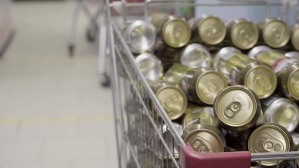 Un montón de latas de cerveza de oro en un carrito de compras en un supermercado — Vídeos de Stock