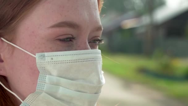 Una chica pelirroja con pecas se quita una máscara médica de la cara. Mujer joven se quita la máscara médica — Vídeos de Stock