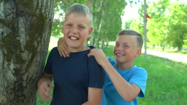 10-12 yaşlarında iki erkek çocuk, kameranın önünde sarılıp oynaşıyorlar. En iyi arkadaşlar. Mutlu bir çocukluk. Hafta sonu dışarıda. — Stok video