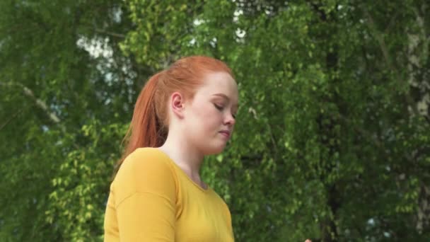 Девушка с рыжими волосами пьет воду из бутылки, останавливаясь во время пробежки на улице — стоковое видео
