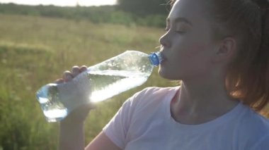 Kızıl saçlı kız dışarıda koşarken duran şişeden su içiyor.