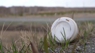 Yolun kenarında çimlerin üzerinde plastik atık var. Kullanılmış kahve fincanı. Kirlilik sorunu.