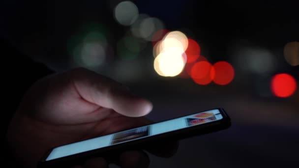 Close-up of hands holding a smartphone. City lights in the background — Stock Video