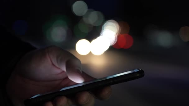 Κοντινό πλάνο των χεριών κρατώντας ένα smartphone. Τα φώτα της πόλης στο παρασκήνιο — Αρχείο Βίντεο