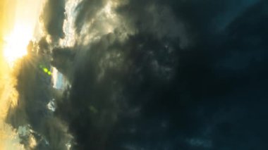 Gün batımında, güneşin aydınlattığı dramatik ağır gri bulutların zaman akışı. Güneşin ışınları ve parlaklığı bulutların arasında