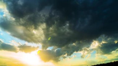 Gün batımında, güneşin aydınlattığı dramatik ağır gri bulutların zaman akışı. Güneşin ışınları ve parlaklığı bulutların arasında