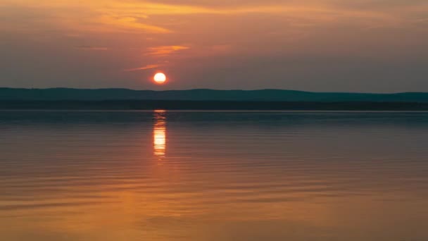 太陽は湖の海岸線の後ろに隠れている。美しい夕日とタイムラプス撮影、夕日と山の湖と澄んだ空の景色 — ストック動画