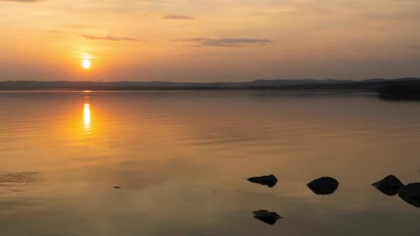 El sol se esconde detrás de la costa del lago. Disparo de lapso de tiempo con una hermosa puesta de sol, una vista de un lago de montaña y un cielo despejado con el sol poniente — Vídeo de stock