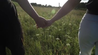Kadınların elleri, arka planda uzun otlarla çevrili vahşi bir çayıra bağlıdır.