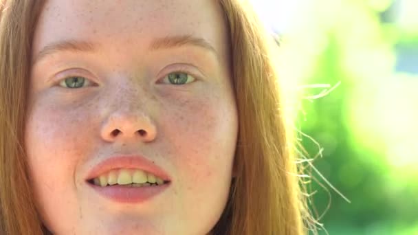 Das Gesicht einer jungen Frau mit roten Haaren und Sommersprossen auf grünem Laub. Natürliche Schönheit mit Sommersprossen — Stockvideo