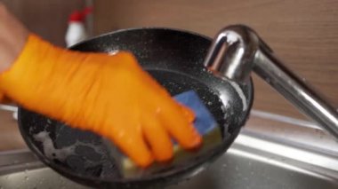 Eldivenli ve süngerli bir adam kirli bir tavayı yıkıyor. Tavayı sünger ve deterjanla yıka.