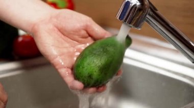 Bir adam musluktan akan suyun altında avokado yıkar..