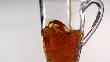 Şeffaf bir bardağı lezzetli bir içecekle doldur. İçki beyaz arka planda şeffaf bir çay bardağına dökülüyor.