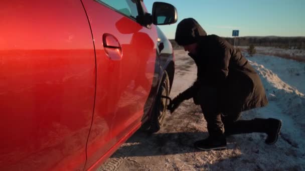 Arrêt d'urgence de la voiture sur le bord de la route par une journée ensoleillée d'hiver. Un homme change une roue sur une voiture. — Video