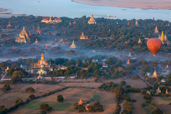 Ранним утром воздушный шар, дрейфующий над храмами Археологической зоны возле реки Иравади в Багане в Мьянме (Бирма)).