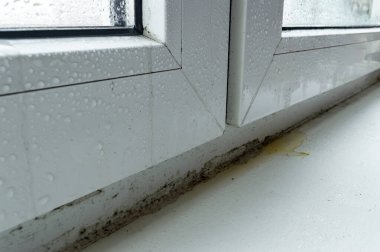 Su damlaları ve küf kaplı kirli beyaz plastik pencere.