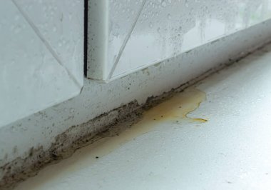 Su damlaları ve küf kaplı kirli beyaz plastik pencere.