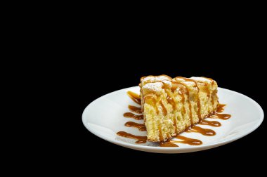 Siyah arka planda beyaz bir tabakta karamelli elmalı turta.