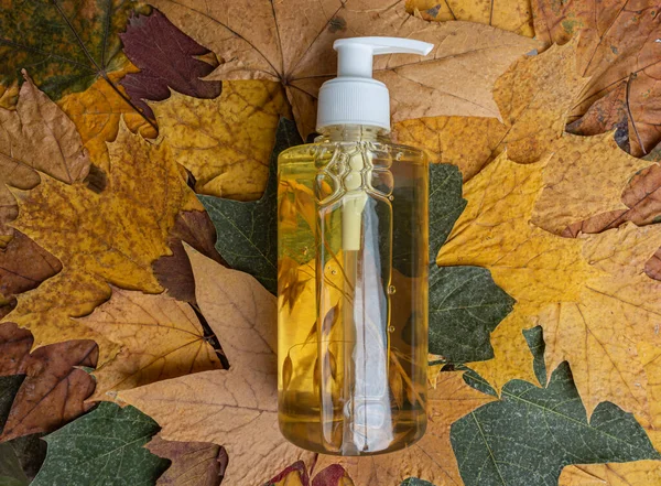 Butelka z dozownikiem i szamponem kosmetycznym na tle jesiennych liści — Zdjęcie stockowe