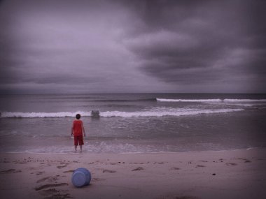 Sahilde oynayan bir çocuk. Yukarıda dramatik bulutlar var. Desenlenmiş resim.