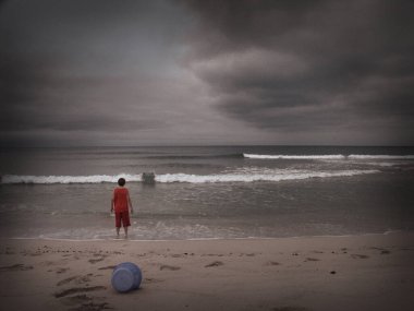 Sahilde oynayan bir çocuk. Yukarıda dramatik bulutlar var. Desenlenmiş resim.