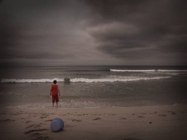 Sahilde oynayan bir çocuk. Yukarıda dramatik bulutlar var. Desenlenmiş resim.