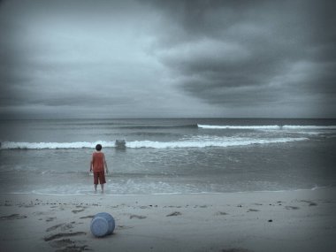 Sahilde oynayan bir çocuk. Yukarıda dramatik bulutlar var. Desenlenmiş resim.