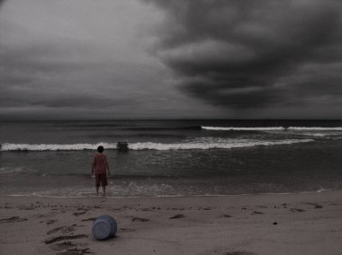 Sahilde oynayan bir çocuk. Yukarıda dramatik bulutlar var. Desenlenmiş resim.