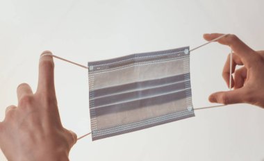 Kadın eli beyaz bir arka planda tıbbi bir maske tutuyor..