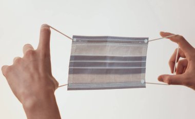 Kadın eli beyaz bir arka planda tıbbi bir maske tutuyor..