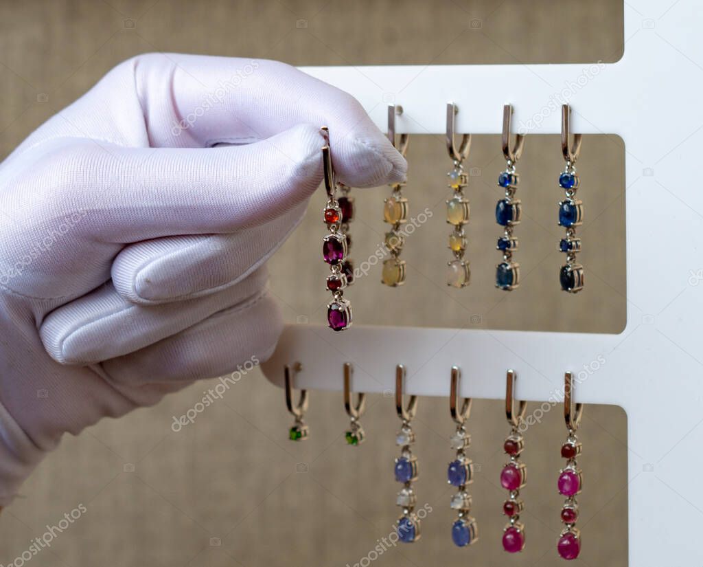 A white-gloved hand holds the earrings. Jewelry made of natural stones.