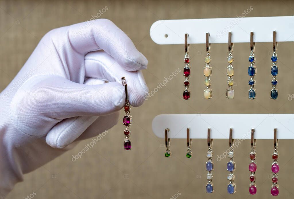 A white-gloved hand holds the earrings. Jewelry made of natural stones.