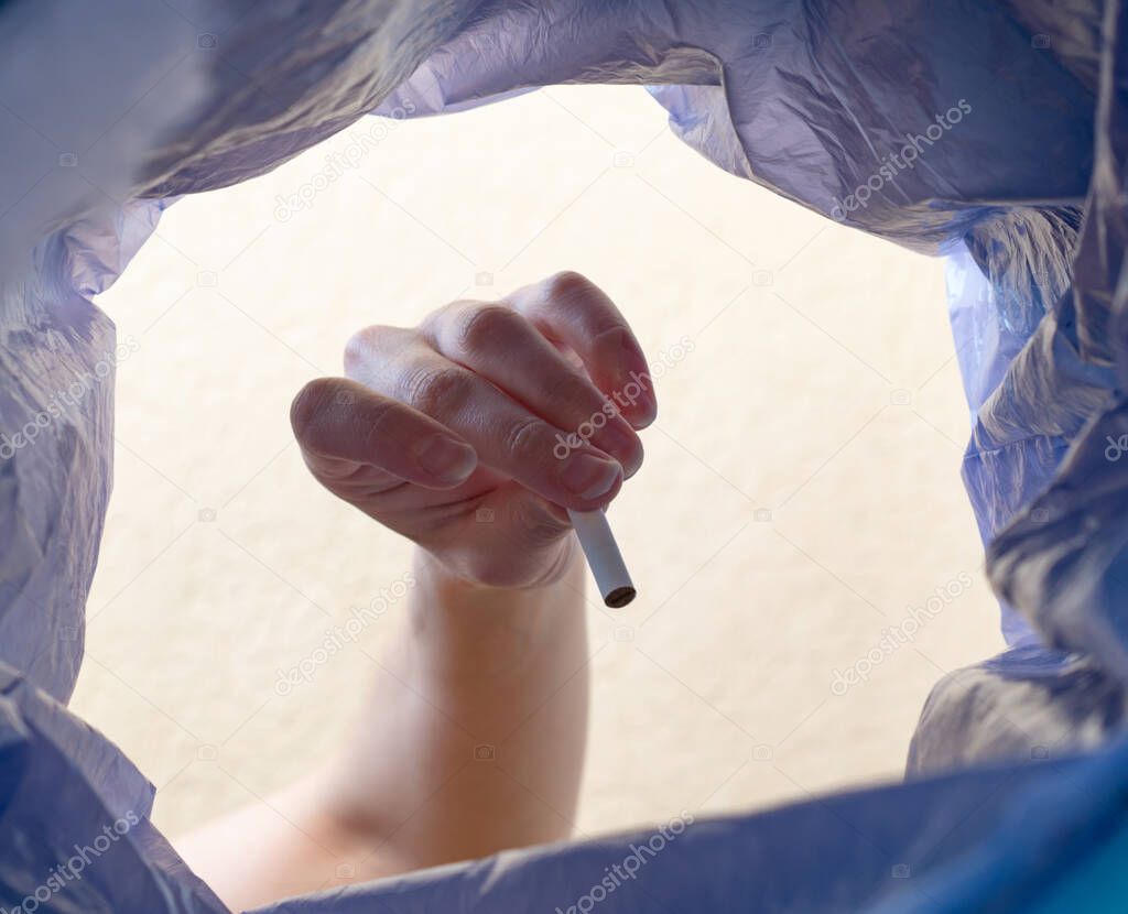 A woman's hand throws a cigarette butt into the trash can.