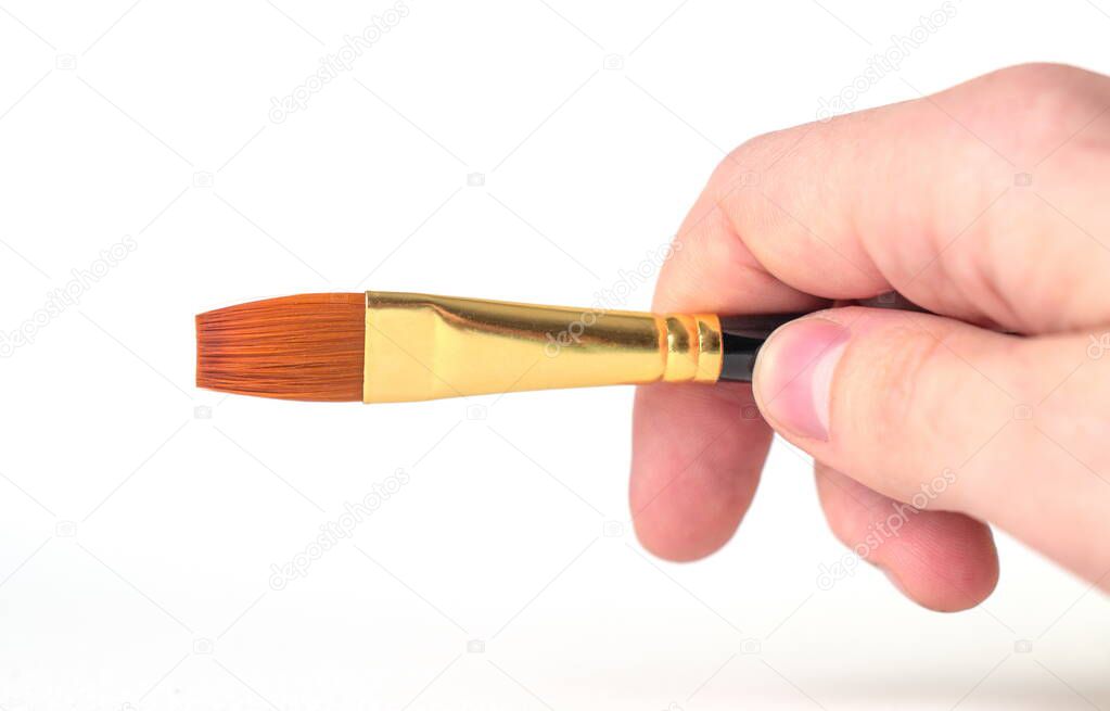 A man's hand holds paintbrush on a white background in close-up. Copy space