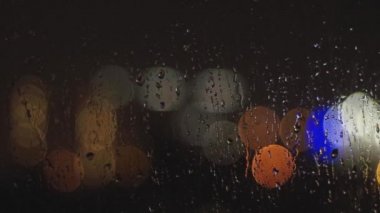  Karanlıkta bulanık ışıkların arkaplanındaki cam üzerindeki yağmur damlalarının yakın plan görüntüsü.