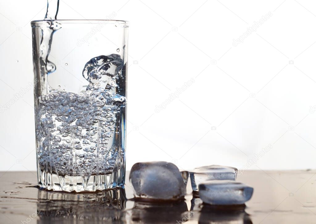 Water is poured into a glass. Melting ice cubes on a wooden table. Close-up. Focus on the water.