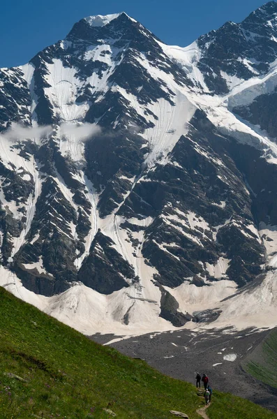 A group of hikers with backpacks are walking along a mountain range against the background of snowy mountains. The concept of traveling to the mountains