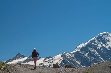 Mavi Gök ve Karla kaplı Dağların Arkasında Dağ yolunda Yürüyen Bir Kadın Görünümü. Yürüyüş konsepti.