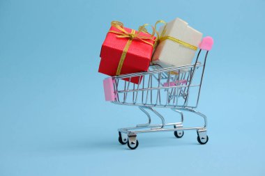 Mavi arka planda hediye kutuları olan alışveriş arabası.