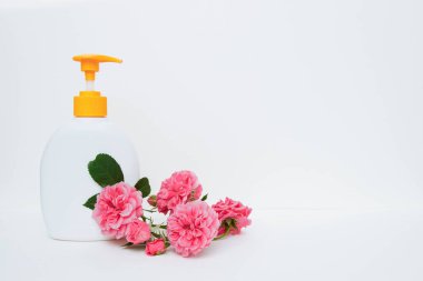 Sıvı sabun ve sarı şeker kutulu boş plastik şişe, beyaz arka planda bir buket pembe gül yazı, vücut bakımı konsepti, yüz derisi, çamaşır ürünleri için boş alan yakın plan görüntüsü.