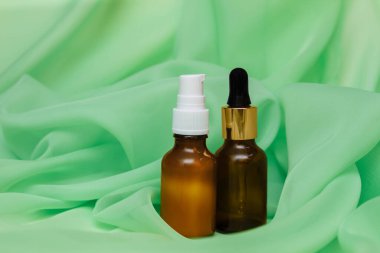 Pipet ve şeker kaplı iki kozmetik cam şişe. Pliseli yeşil ipek kumaş, fotokopi alanı, yaşlanma önleyici ve akne cilt bakımı. Ürün reklam şablonu.