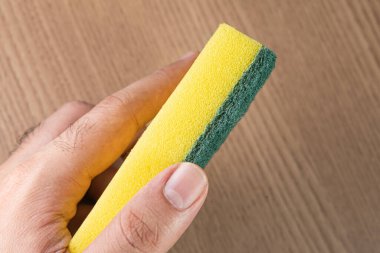 Ahşap arka planda mutfak süngeri tutan adam.