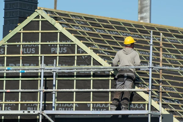 Artigiano che lavora su un tetto da un'impalcatura. Indossa un casco di protezione giallo. . — Foto Stock