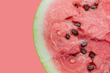 Pembe arka planda siyah çekirdekli olgun karpuzun yarısı.