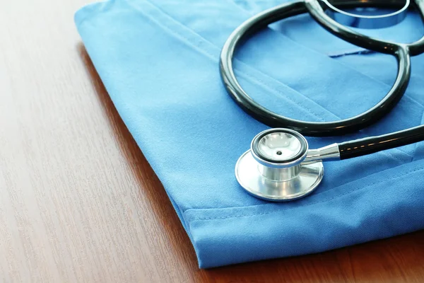 Estetoscopio con abrigo médico azul sobre mesa de madera y fondo — Foto de Stock